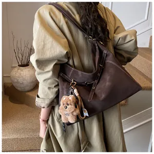 Detailed view of a retro brown slouchy shoulder bag with cute bear charm and contrast stitching.