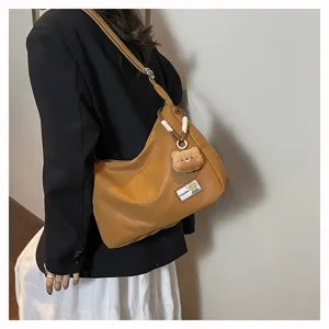 Retro soft leather dumpling shoulder bag with cute bear pendant for daily commuting.