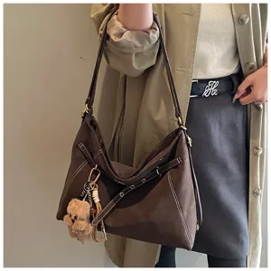 Brown vintage shoulder tote bag detail, featuring white stitching and bear pendant.