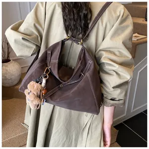 Detailed view of dark brown retro leather tote backpack with cute bear keychain and white stitching.