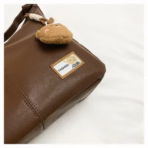 Brown soft leather dumpling shoulder bag detail close-up, featuring cute bear pendant.