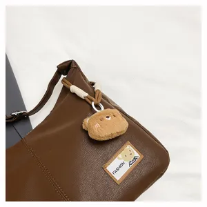 Retro soft leather slouchy shoulder bag detail with cute bear plush pendant and chic fashion label.