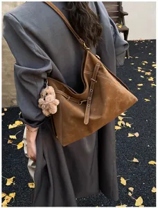 Detail view of brown suede shoulder hobo bag with contrast stitching and teddy bear charm.
