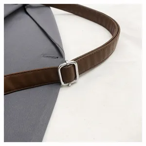 Close-up detail of the adjustable brown leather strap and silver metal buckle on grey bag.