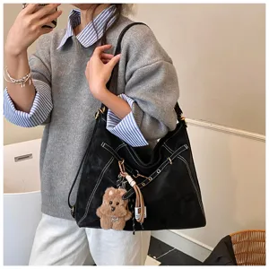 Black suede tote bag with contrast stitching and cute bear charm for women daily use.