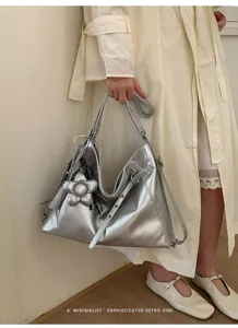 Primo piano della borsa a tracolla tote metallica argentata elegante con ciondolo floreale.