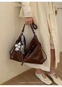 Dettaglio della borsa tote marrone retro con ciondolo floreale argentato e texture in pelle.