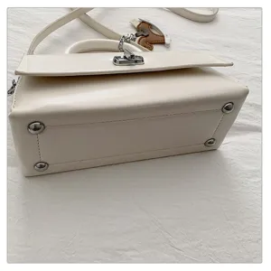 Detailopname van witte lederen schoudertas met metalen sluiting en beschermnoppen.