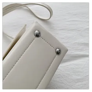Minimalistische witte schoudertas detail, glad leer, metalen klinknagels en fijne stiksels.