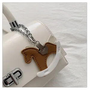 Close-up van het chique witte lederen handtasdetail met schattige schommelpaardhanger.