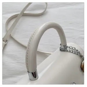 Close-up detail van witte leren handtasgreep, met glanzende metalen ringen en kettingdecor.