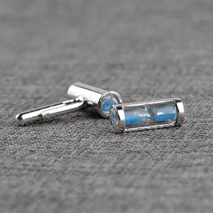 Detailed close-up of silver-tone metal hourglass cufflinks with blue sand for men shirts.