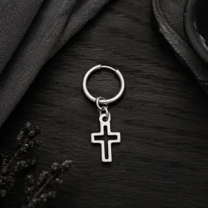 Gros plan détaillé d'une boucle d'oreille créole avec pendentif croix en métal argenté.