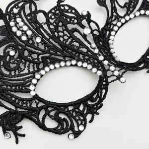 Black lace masquerade mask detail close-up showing intricate embroidery and shining rhinestones.