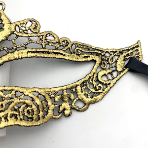 Close-up detail of gold lace masquerade mask, showing intricate embroidery texture and ribbon.