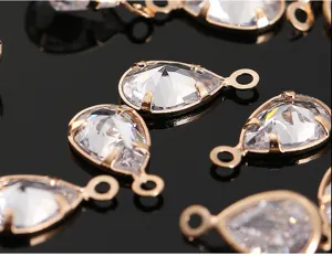 Primer plano de colgante de dije de circón de cristal en forma de gota con piedra y aro dorado.