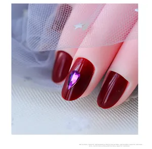 Primer plano detallado de uñas postizas rojo oscuro con brillante strass en gota morada.