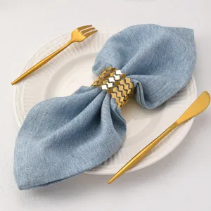 Dettaglio dell'anello portatovagliolo in metallo dorato ondulato con elegante tovagliolo blu.