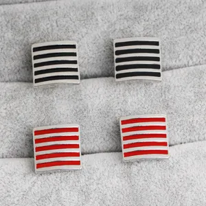 Close up detail shot of square metal cufflinks with black and red striped enamel design on tray.