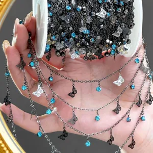 Close-up detail of DIY black chain with blue rhinestones and delicate metal butterfly charms.
