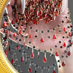 Gros plan détail chaîne de bijoux DIY en cristal goutte rouge gothique sombre.