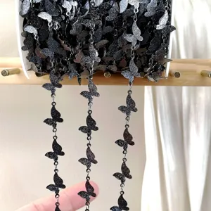 Close-up detail of black butterfly metal chain roll, dark style DIY apparel accessory part.