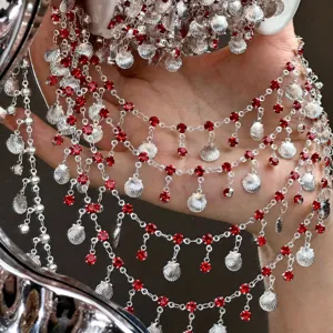 Close-up of DIY silver chain with red rhinestones and shells for handmade doll clothes.