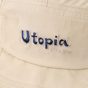 Primer plano detallado de gorra de béisbol impermeable beis con bordado azul Utopia.