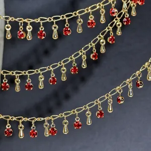 Détail en gros plan d'une chaîne DIY dorée avec strass rouges et pendentifs pour les cheveux.