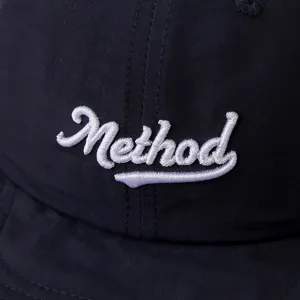 Vista cercana de los detalles de letras Method bordadas en blanco en la gorra negra.