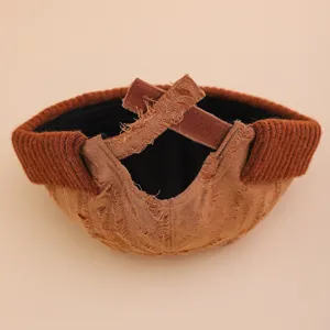 Vista detallada del gorro docker marrón desgastado con borde de punto acanalado y correa cruzada.