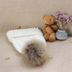 Detailed view of cozy white winter knitted beanie hat with fluffy fur pom pom decoration.