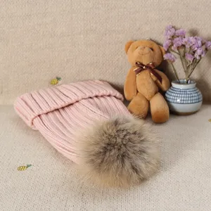 Pink knit beanie hat featuring a fluffy fur pom-pom detail, soft winter warm headwear.