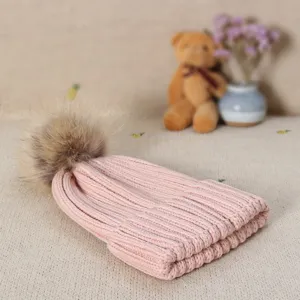 Close up detail of women winter pink knitted beanie hat with fluffy faux fur pom cozy.