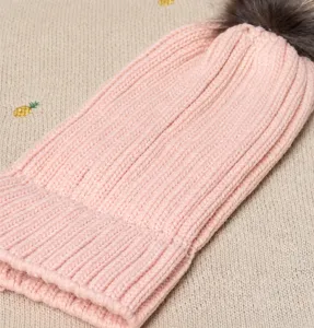Pink knitted beanie winter warm hat with fur pom pom, cozy ribbed knit detail closeup.