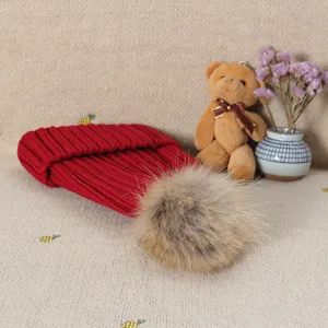 Red knitted beanie winter hat with fluffy fur pom pom warm wool cap for women detail view.