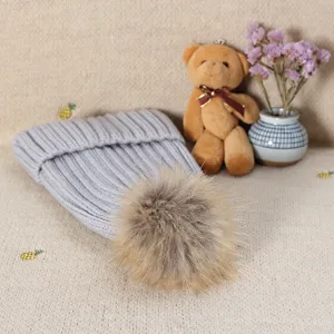 Cozy grey knitted winter beanie featuring a fluffy faux fur pom-pom. Soft and warm accessory.