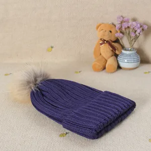 Cozy winter knitted hat with fluffy fur pom pom in deep purple, casual warm ladies cap.