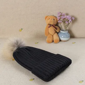 Black knitted beanie hat with fluffy fur pom-pom detail, cozy winter cold weather accessory.