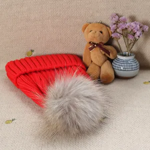 Detail view of a red winter knit beanie hat with a fluffy faux fur pom-pom, cozy and warm.