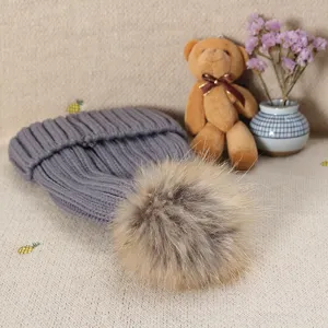 Detail view of a cozy gray knit winter beanie hat featuring a fluffy furry pom-pom accent.