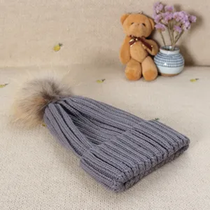 Grey knit beanie hat with fluffy fur pom pom winter warm knitted cap detail view.