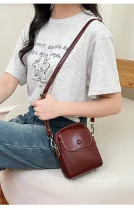Detail view of dark red leather crossbody phone bag worn by model, showcasing metal strap and snap.
