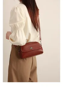 Close-up of vintage oil wax leather crossbody bag with metal button detail and contrast stitching.