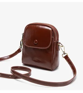 Brown leather small crossbody bag detail, featuring flap button closure and double zippers.