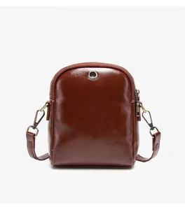 Brown leather mini crossbody bag detail, featuring metallic zipper, ring accent and strap hooks.