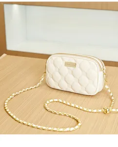 Detailed view of the chic beige quilted crossbody bag with gold chain and metal brand plate.