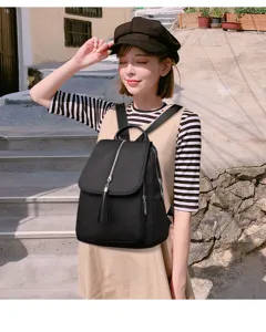 Close-up detail of a stylish black backpack with tassel zipper outdoors on stone steps.