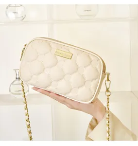 Detailed view of off-white quilted shoulder bag with gold chain strap and metal logo plate.