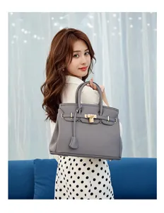 Detailed view of grey textured leather handbag with metal lock and top handles in indoor scene.